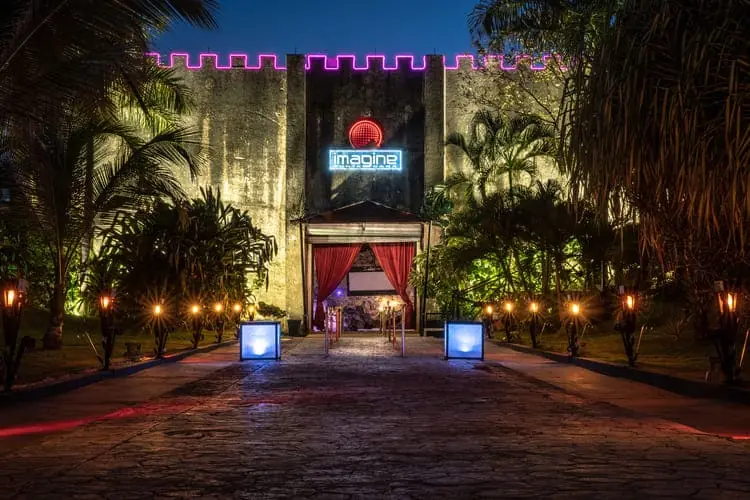 entrance facade of Imagine Punta Cana nightclub at night with torches lighting the access path
