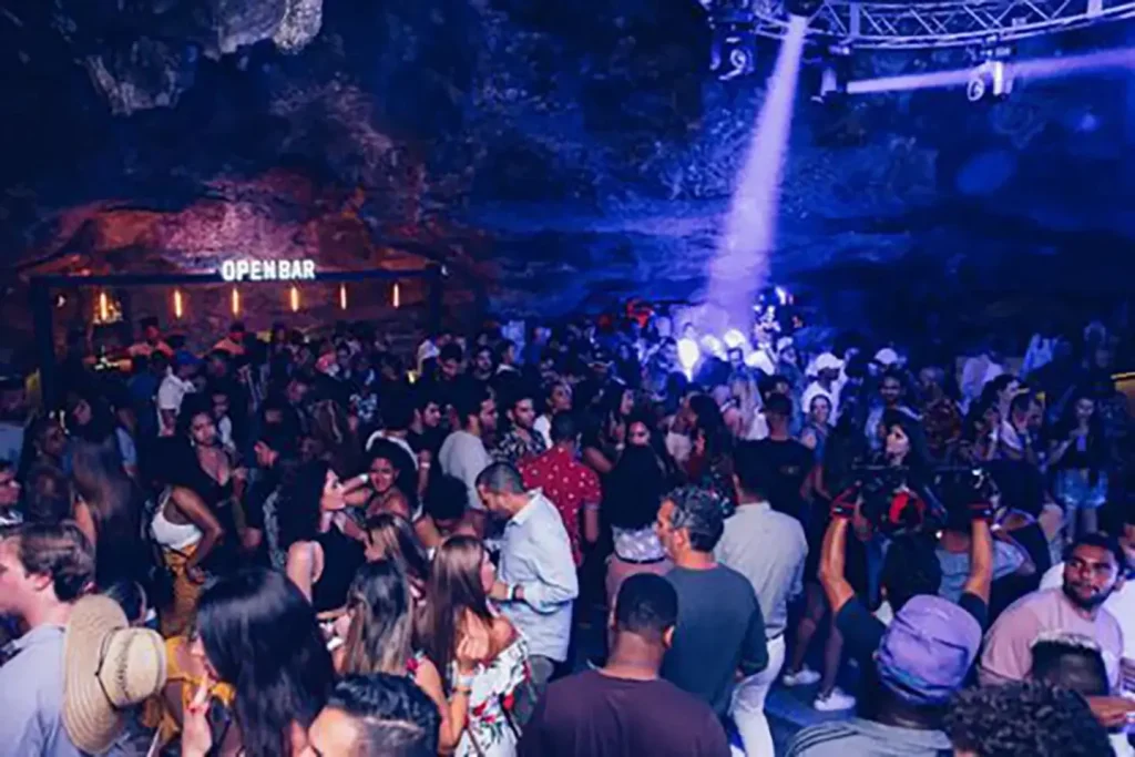 Pista de dança cheia na Sala Universo da Imagine Punta Cana, com estrutura de Open Bar iluminada ao fundo dentro da caverna natural