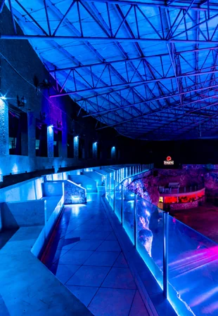 Corredor elevado do Imagine Punta Cana com guarda-corpos de vidro e iluminação azul e roxa dentro da caverna natural — espaço para eventos
