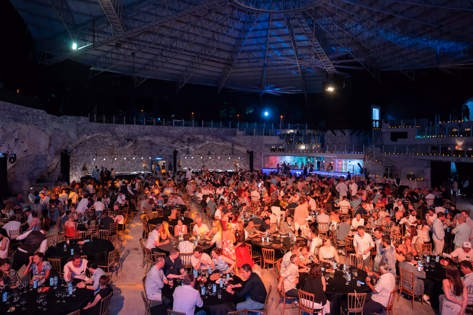 Público em evento privado no Imagine Punta Cana, com mesas e palco iluminados dentro da caverna natural